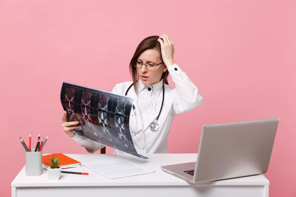 female doctor sit desk work computer with medical document hold x ray hospital isolated pastel pink wall background woman medical gown glasses stethoscope healthcare medicine concept